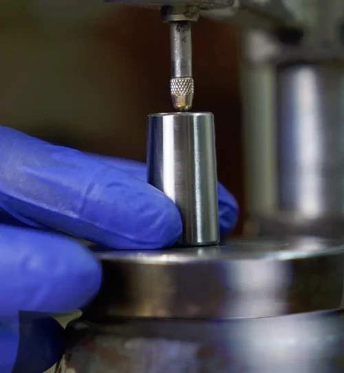 close-up of a hardness testing process on a metal componentnwith a technician wearing blue gloves.